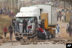 Rioters cling to the front of a lorry as they clash with Zimbabwean police in Harare, Monday, July, 4, 2016