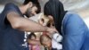 Parents from Syria use water to cool their baby as they wait to cross the border from the northern Greek town of Idomeni to southern Macedonia, Sept. 3, 2015.