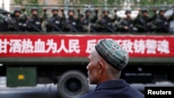 FILE - A Uighur man looks on as a truck carrying paramilitary policemen travel along a street during an anti-terrorism oath-taking rally in Urumqi, Xinjiang Uighur Autonomous Region.