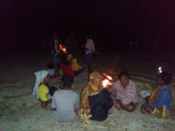 Warga komunitas adat Besipae, Rabu (19/8) duduk di atas tanah dengan penerangan api unggun sambil memeluk anak mereka yang tertidur. (Foto: Martheda Esterlina Selan)