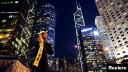 A woman holds a banner and a helmet, symbols of the pro-democracy movement, as she has her picture taken in part of Hong Kong's financial central district occupied by protesters, Oct. 29, 2014. 