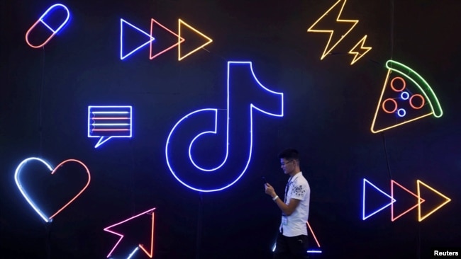 在杭州国际智能产品博览会期间，一位男士拿着手机走过字节跳动公司的TikTok与抖音应用软件的标识。(2019年10月18日)
