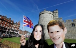 People wearing face masks of Britain's Prince Harry and Meghan Markle pose for a photograph outside Windsor Castle in Windsor, England, May 14, 2018.