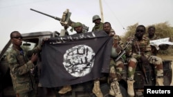 FILE - Nigerian soldiers hold up a Boko Haram flag that they had seized in the recently retaken town of Damasak, Nigeria.