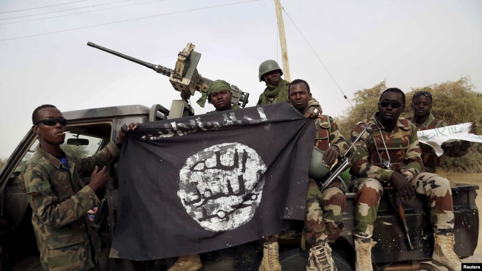 FILE- Nigerian soldiers hold up a Boko Haram flag that they had seized in the recently retaken town of Damasak, Nigeria.