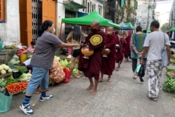 Buddhist monks collect alms from people during their morning walk at the Bogalay Zay Market in Botahtaung township in Yangon, Myanmar, Nov. 12, 2021.