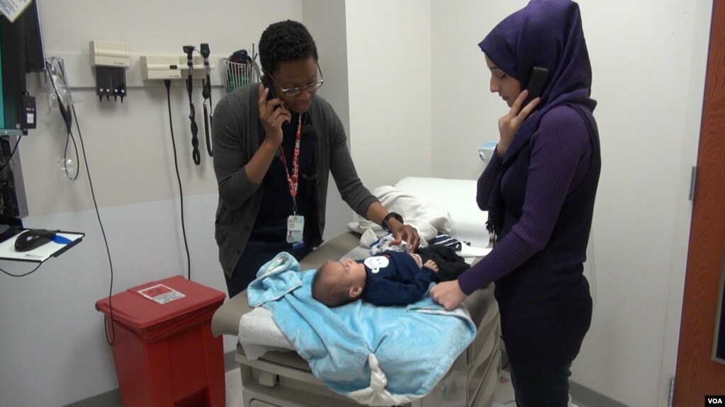 A mother listens to an interpreter by telephone as her baby is examined at the International Family Medicine Clinic in Charlottesville, Virginia, (J.Soh/VOA)