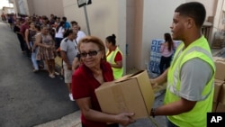 Doris Martínez receives supplies and water from municipal staff outside the City Hall in Morovis, Puerto Rico, Dec. 21, 2017. Over 30,000 residents of that mountain town wait for the restoration of electric power service, one of the last municipalities of Puerto Rico that remains completely in the dark more than three months after the passage of Hurricane Maria. 