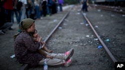 An Afghan refugee woman holding her daughter rests while waiting to board a train heading to the Austrian border, in Roszke, southern Hungary, Sept. 14, 2015. 