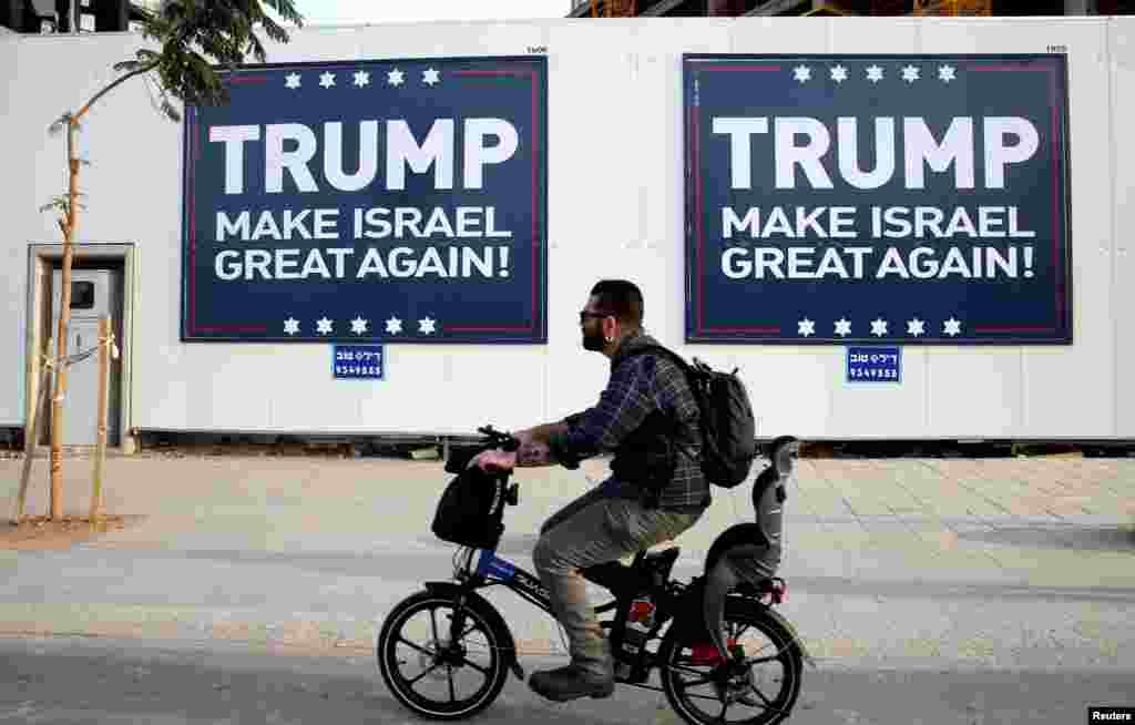 A man cycles past signs bearing the name of U.S. President-elect Republican Donald Trump in Tel Aviv, Israel.