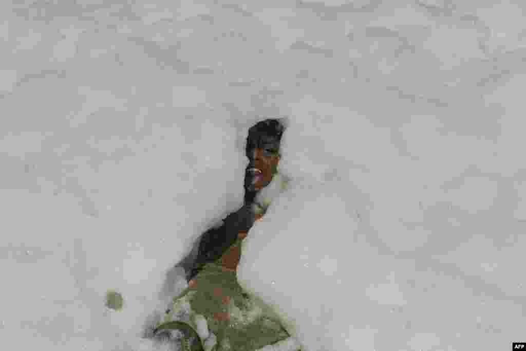 A youth plays in foamy discharge, caused by pollutants, as it mixes with the surf at a beach in Chennai, India.