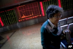 A woman walks past an electronic board displaying stock prices as she leaves a brokerage house in Beijing, Monday, Jan. 4, 2016.
