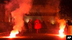 Covered with red paint riot police officers stand among flares thrown by protesters during a rally outside the Greek Parliament in Athens, Jan. 15, 2018.
