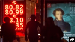 People walk past a currency exchange display board showing the value of the Russian ruble against the U.S. dollar and the euro, in Moscow, Russia, Jan. 20, 2016.