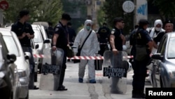 Riot police stand guard as forensic experts in white suits search for evidence on a street behind the headquarters of the co-ruling Socialist PASOK party in Athens, May 25, 2014. 