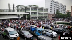 FILE - Workers protest during a strike as police stand guard at the factory area of Yue Yuen Industrial, in Dongguan, Guangdong province, April 18, 2014.