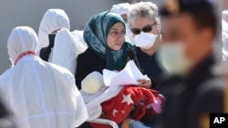 A migrant woman holding a child receives medical treatment after debarking an Italian Navy ship in Sicily, Italy, Saturday, April 18, 2015. (AP PHOTO)