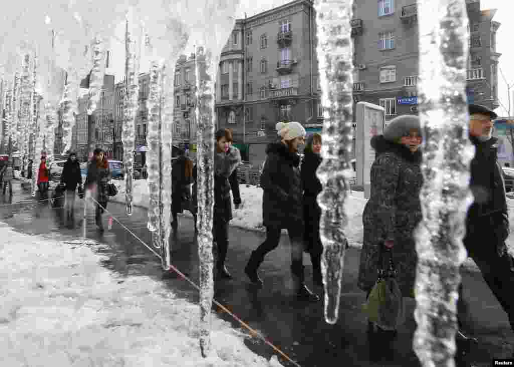 People walk past icicles, which hang from the roof of a building in a street in central Kyiv, Ukraine.