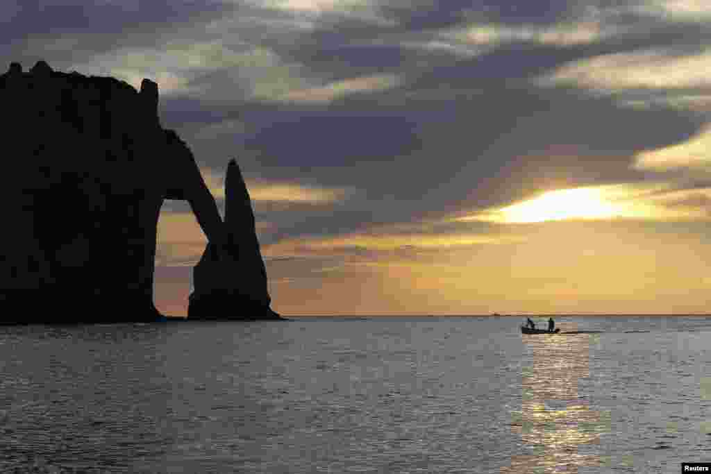 French fishermen are seen going back to the beach during sunset near the 'Porte d'Aval', a famous arch of the Etretat's cliffs in western France, Oct. 11, 2014.