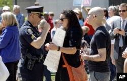 FILE - A police officer confronts a woman holding a sign at the North Carolina State Capitol in Raleigh, N.C., April 11, 2016, during a rally in support of a law that blocks rules allowing transgender people to use the bathroom aligned with their gender identity.