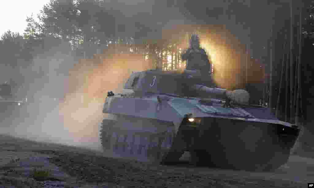 A soldier surrounded by smoke and dust sits on top of a Belarus army self-propelled artillery tank as they head to the rehearse for the Independence Day military parade in outskirts of Minsk.