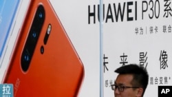 បុគ្គលិក​ម្នាក់​ឈរ​នៅ​ខាង​ក្រៅ​ហាង​លក់​ទូរស័ព្ទ Huawei ក្នុង​ទីក្រុង ប៉េកាំង ថ្ងៃ​អង្គារ ទី៣០ ខែកក្កដា ឆ្នាំ២០១៩។ (AP)