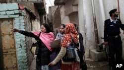 In this Jan. 30, 2013 photo, a Pakistani police officer, right, guards a group of health workers going from house to house to give polio vaccines to children in Islamabad, Pakistan.