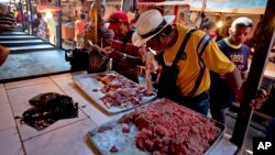 A customer smells a piece of spoiled meat at a market in Maracaibo, Venezuela, Aug. 19, 2018. Venezuelans are lining up at one of the country's largest markets to buy spoiled meat. At bargain prices, it's the only way they can afford beef.