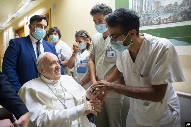 Paus Fransiskus disambut oleh staf rumah sakit saat dia duduk di kursi roda di dalam Poliklinik Agostino Gemelli di Roma, Minggu, 11 Juli 2021, di mana dia dirawat untuk operasi usus. (Media Vatikan melalui AP)