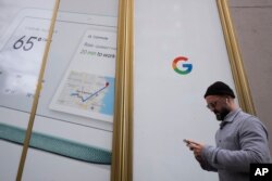 A man using a mobile phone walks past Google offices, Monday, Dec. 17, 2018, in New York. (AP Photo/Mark Lennihan)