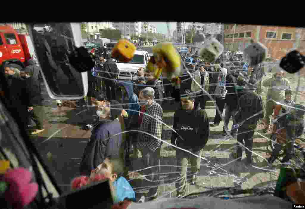 Palestinians are seen through a damaged windscreen of a bus as they gather at the scene of an Israeli airstrike, northern Gaza Strip, Jan. 19, 2014. 