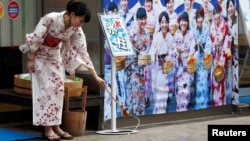 A woman wearing a Yukata, or summer kimono, splashes water onto the hot asphalt in an old Japanese tradition called Uchimizu ritual, meant to cool down the air as the water evaporates, outside a pachinko game parlor in Tokyo, July 23, 2018. 