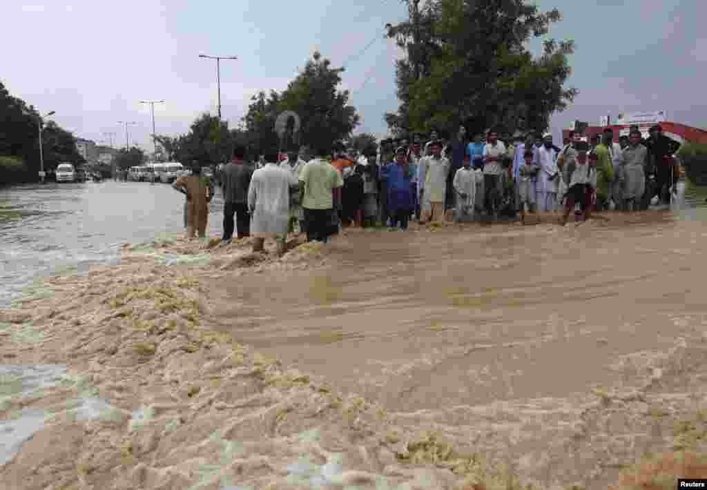 Residents wait to cross a flooded road on the outskirts of Karachi, August 4, 2013. At least a dozen people were killed in accidents caused by torrential rain which hit different parts of the port city of Karachi.