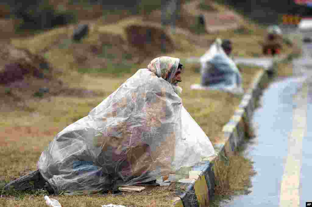 Men wait to receive alms as they cover themselves with plastic sheets in a rain in Islamabad, Pakistan.