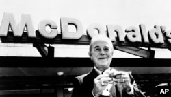 Ray A. Kroc, founder of McDonald's Corporation, is shown holding a hamburger in front of a McDonald's restaurant at an unknown location in this undated photo.