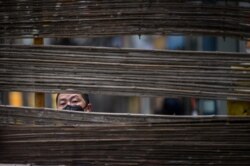 A man wearing a face mask looks through a barrier in a neighborhood in Wuhan, the central Chinese city where the coronavirus first emerged last year, in central Hubei province.