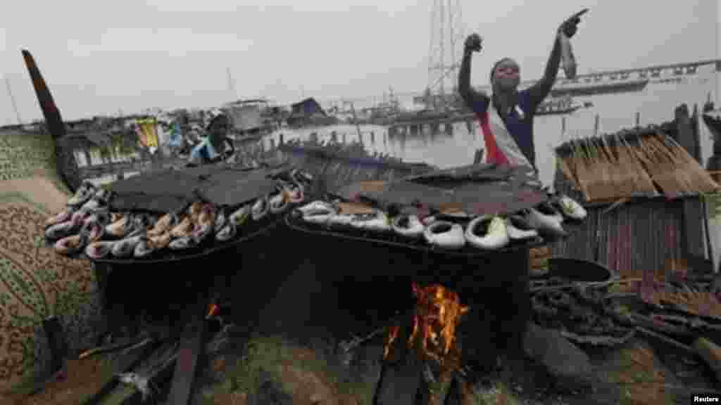 A woman gestures as she smokes fish at her demolished illegal stilt house in Legas.