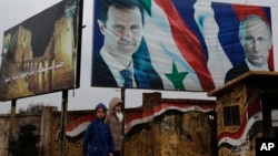 FILE - Syrians walk past posters of Syrian President Bashar al-Assad and Russian President Vladimir Putin, in Aleppo, Syria, Jan. 18, 2018.
