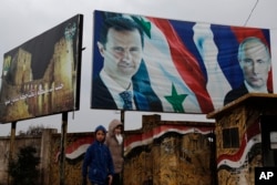 FILE - Syrian walk by posters of Syrian President Bashar al-Assad and Russian President Vladimir Putin in Aleppo, Syria, Jan. 18, 2018.