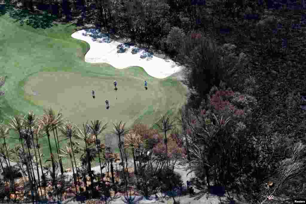 Golfers are seen on the green next to a bushfire-damaged area in Peregian Springs on the Sunshine Coast, Australia.