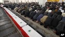 Syrian mourners pray in front of the coffins of 11 Syrian police officers who were among those killed in an explosion in the Midan district of Damascus Friday, during a mass funeral at Al-Hassan mosque in the Syrian capital Saturday, January 7, 2012.