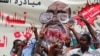 Protesters shout slogans by a banner depicting former Sudanese President Omar al-Bashir, in front of the Defense Ministry in Khartoum, Sudan, April 19, 2019. 