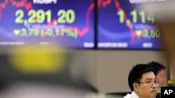A currency trader watches the computer monitors near the screens showing the Korea Composite Stock Price Index (KOSPI), left, and the foreign exchange rate between U.S. dollar and South Korean won at the foreign exchange dealing room in Seoul, South Korea