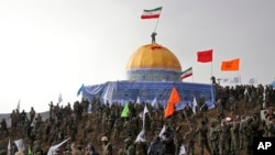 Members of the Basij, the paramilitary unit of Iran's Revolutionary Guard, gather around a replica of Jerusalem's gold-topped Dome of the Rock mosque as one of them waves an Iranian flag from on top of the dome during a military exercise, outside Qom, Iran, Nov. 20, 2015.