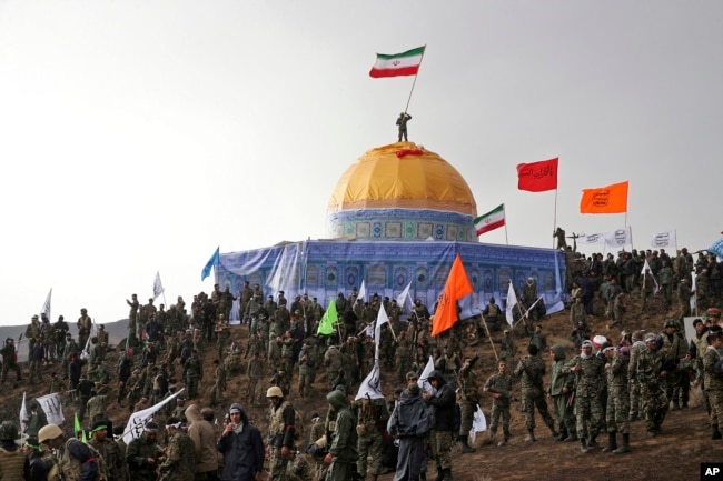 FILE - Members of the Basij, the paramilitary unit of Iran's Revolutionary Guard, gather around a replica of Jerusalem's gold-topped Dome of the Rock mosque as one of them waves an Iranian flag from on top of the dome during a military exercise, Nov. 20, 2015.