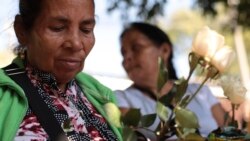 Juana Bonilla, de 66 años, sostiene rosas blancas mientras espera con sus familiares para recibir seis pequeños ataúdes que contienen los restos de sus familiares que fueron asesinados en una masacre de 1982.