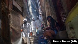 Volunteers spray disinfectant in an alley to help contain the spread of the new coronavirus at the Santa Marta slum in Rio de Janeiro, Brazil, Saturday, Nov. 28, 2020.