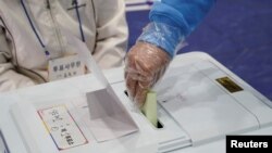 Seorang pemilih mengenakan sarung tangan plastik memasukkan surat suara di tempat pemungutan suara dalam pemilu legislatif di tengah pandemi virus corona di Seoul, Korea Selatan, 15 April 2020. (Foto: Reuters)