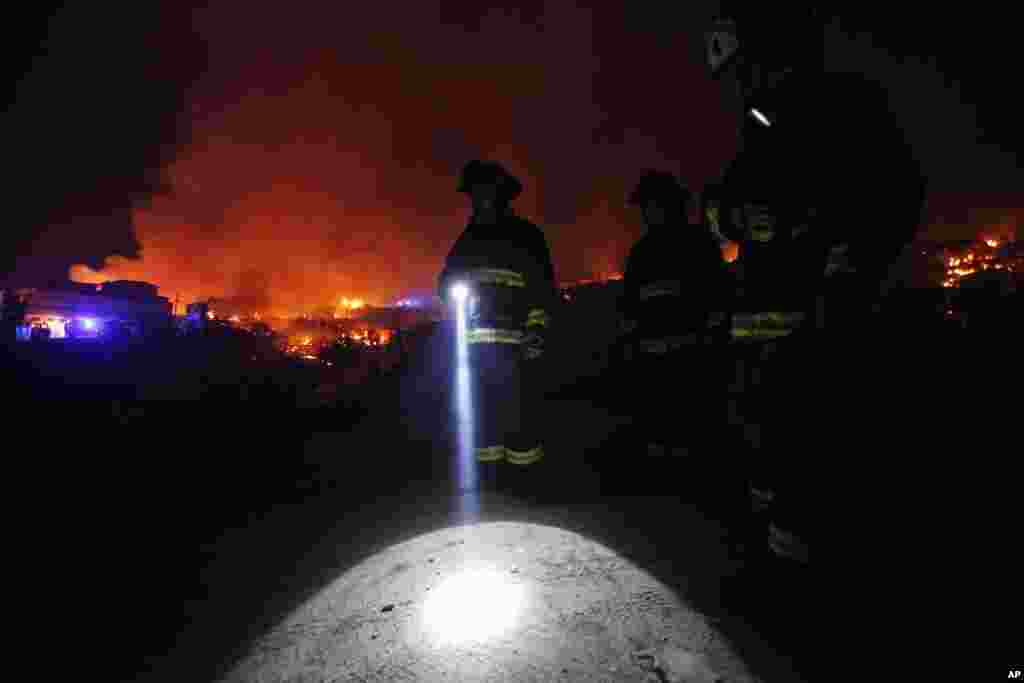 A firefighter shines a flashlight as he stands with others near burning homes as a forest fire rages towards urban areas in the city of Valparaiso, Chile.
