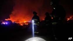 A firefighter shines a flashlight as he stands with others near burning homes as a forest fire rages towards urban areas in the city of Valparaiso, Chile, Sunday April 13, 2014.